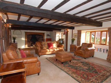 A living room with leather sofas a patterned rug wooden beams on the ceiling and a fireplace at Surridge Farmhouse in Waterrow