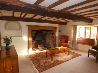 A living room with wooden beams a stone fireplace a wooden coffee table and armchairs at Surridge Farmhouse in Waterrow
