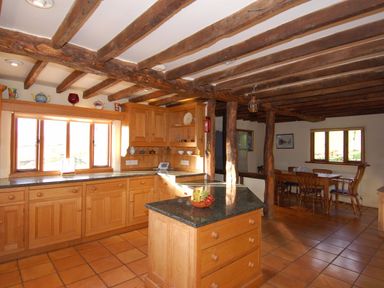 A kitchen with wooden cabinets a countertop island and a dining table in the background at Surridge Farmhouse in Waterrow