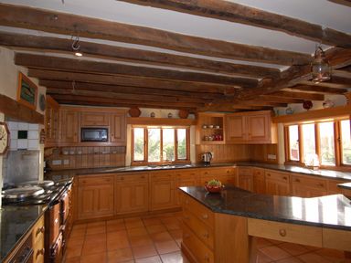 A kitchen with wooden cabinets granite countertops central island and exposed wooden beams at Surridge Farmhouse in Waterrow