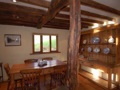 A dining room with a wooden table and chairs a wooden cabinet with plates on shelves and a window at Surridge Farmhouse in Waterrow