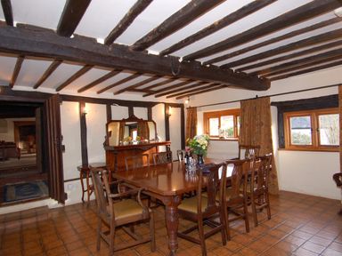A dining room with wooden table and chairs wooden beams on ceiling and windows with curtains at Surridge Farmhouse in Waterrow