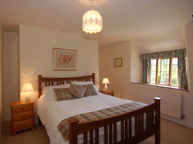 A bedroom with a wooden bed frame two bedside tables with lamps and a window with floral curtains at Surridge Farmhouse in Waterrow
