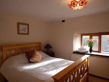A bedroom with a wooden bed two patterned pillows a vase with flowers and folded towels on the windowsill at Surridge Farmhouse in Waterrow