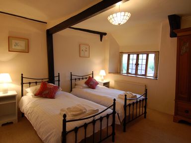 A bedroom with two single metal frame beds bedside tables lamps a window and a wooden wardrobe at Surridge Farmhouse in Waterrow