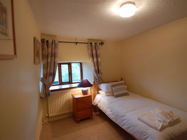 A small bedroom with a single bed bedside table with lamp window with polka dot curtains at Surridge Farmhouse in Waterrow