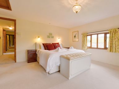 A bedroom with a bed and red pillows a bench at the foot of the bed a window with curtains and bedside tables at Surridge Farmhouse in Waterrow