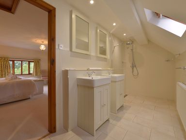 A bathroom with two sinks mirrors and a shower area with a window and a view of a bedroom at Surridge Farmhouse in Waterrow