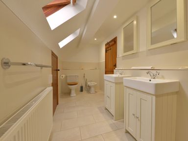 A bathroom with two sinks two mirrors a toilet a bidet wooden door and skylights at Surridge Farmhouse in Waterrow