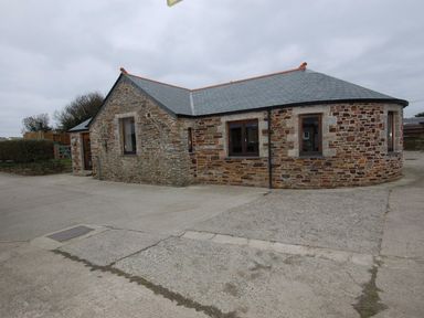 A single story stone house with multiple windows and a gray roof on a concrete driveway at Hideaway in Tintagel