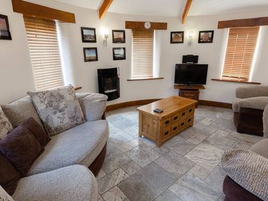 A seating area with sofas a wooden coffee table a television and windows with blinds at Hideaway in Tintagel