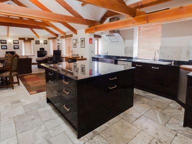 An open plan kitchen and living area with wooden ceiling beams a black kitchen island dining table and chairs and a television at Hideaway in Tintagel
