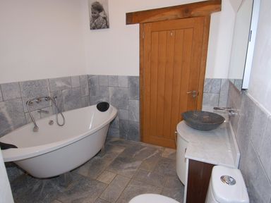 A bathroom with a freestanding bathtub a round sink a toilet and a wooden door at Hideaway in Tintagel
