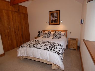A bedroom with a bed against the wall with patterned pillows and blanket two wooden bedside tables a wooden wardrobe and horse artwork above the bed at Hideaway in Tintagel