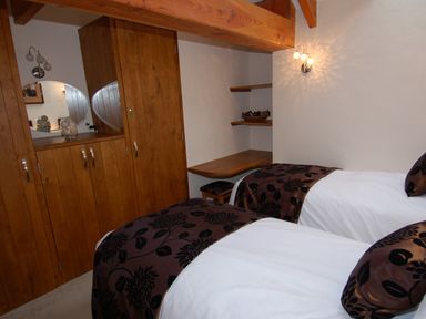 A bedroom with two single beds a wooden wardrobe and a corner wooden desk at Hideaway in Tintagel