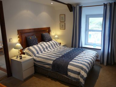 A bedroom with a double bed with striped bedding two bedside tables with lamps and a window with striped curtains at The Keep Pot in Port Isaac