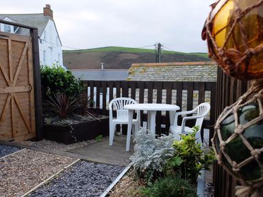 An outdoor patio with two white plastic chairs and a round table near a wooden fence and plants at The Keep Pot Port Isaac