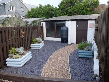 A garden with a gravel path flanked by raised planters and a shed at The Keep Pot in Port Isaac