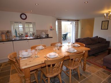 A kitchen and dining area with a wooden table set for six people next to a sofa and sliding doors at The Barn in Tregoodwell