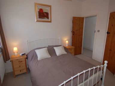 A bedroom with a double bed with gray bedding two bedside tables two lamps and wooden doors at The Barn in Tregoodwell