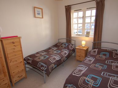 A bedroom with two single beds a wooden chest of drawers and a bedside table with a lamp at The Barn in Tregoodwell