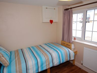 A small bedroom with a single bed covered with striped blue and brown bedding a window with a purple curtain and a radiator below at The Barn in Tregoodwell