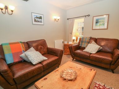 A sitting room with two brown leather sofas a wooden coffee table and a side table with a lamp at Robyn Cottage in Otterton