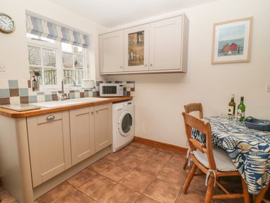 A kitchen with wooden cabinets a washing machine a microwave and a small dining table with chairs at Robyn Cottage in Otterton