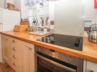 A kitchen counter with a stove kettle oven and utensils by a window at Robyn Cottage in Otterton