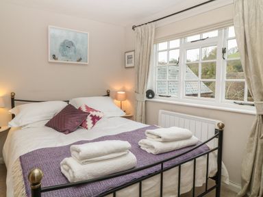 A bedroom with a bed with white sheets and purple cushions and a purple throw with folded white towels on it at Robyn Cottage in Otterton