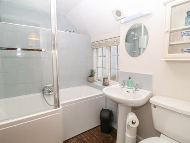 A bathroom with a bathtub and shower, a sink with a mirror above, a toilet, and a window with a roman blind at Robyn Cottage in Otterton