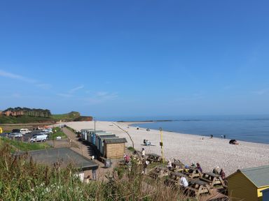 A pebble beach with beach huts parking and picnic tables by the sea at Robyn Cottage in Otterton