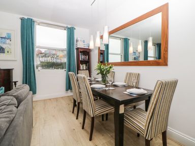 A dining room with a dark wood table set for six with striped chairs a large mirror on the wall and teal curtains at Quayside Lookout in Brixham