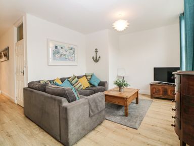 A living room with a gray sofa and colorful cushions a wooden coffee table a television on a wooden stand and a decorative anchor on the wall at Quayside Lookout in Brixham