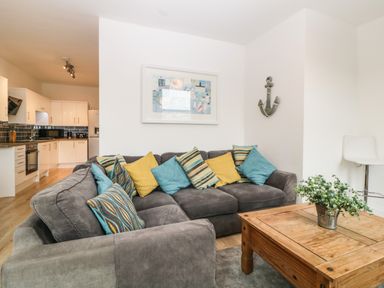 A living room with a gray sofa with multiple cushions and a wooden coffee table with a plant at Quayside Lookout in Brixham