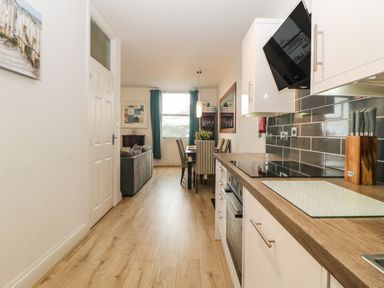A kitchen with wooden countertops and white cabinets leading to a dining area with a table and chairs and a living room with a gray sofa at Quayside Lookout in Brixham