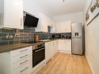 A kitchen with white cabinets grey tiled backsplash wooden countertops oven refrigerator and microwave at Quayside Lookout in Brixham