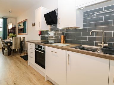 A kitchen with white cabinets black tiled backsplash wooden countertop and a dining area with a table and chairs at Quayside Lookout in Brixham