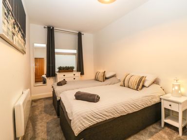 A bedroom with two single beds a small white bedside table with a lamp a chest of drawers with a plant and mirror at Quayside Lookout in Brixham