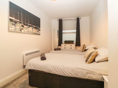 A bedroom with two beds pillows and folded towels a dresser under a window with dark curtains and a wall painting at Quayside Lookout in Brixham