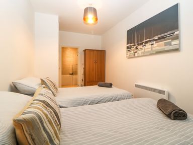 A bedroom with two single beds a wooden wardrobe and an open door to a bathroom at Quayside Lookout in Brixham