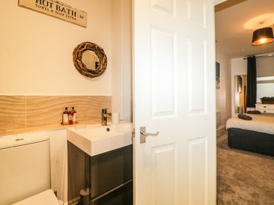 A bathroom with a toilet sink and mirror partially open door to a bedroom with a bed and bedside table at Quayside Lookout in Brixham