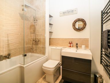 A bathroom with a bathtub shower combination toilet sink with cabinet and a round wall mirror at Quayside Lookout in Brixham