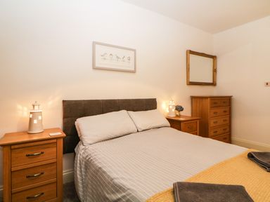 A bedroom with a double bed flanked by wooden bedside tables and a dresser with a mirror at Quayside Lookout in Brixham