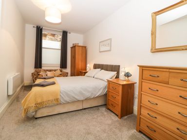 A bedroom with a bed two bedside tables a chest of drawers armchair and window with curtains at Quayside Lookout in Brixham