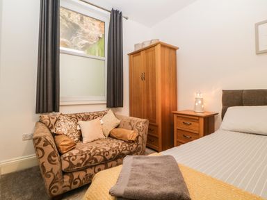 A bedroom with a patterned sofa pillows wooden wardrobe bedside table bed with striped bedding and a window with dark curtains at Quayside Lookout in Brixham