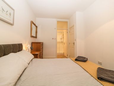A bedroom with a bed striped bedspread two gray towels a wooden chest of drawers a mirror on the wall and a doorway leading to a bathroom at Quayside Lookout in Brixham