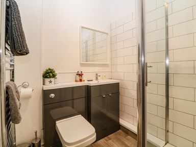A bathroom with a toilet, vanity with sink, mirror, glass shower enclosure, towels on a radiator, and tiled walls at Quayside Lookout in Brixham