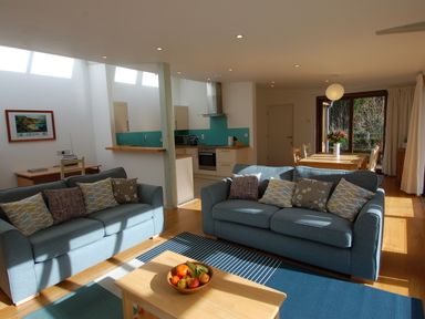 A living room with two blue sofas and a coffee table with fruit a kitchen with turquoise backsplash and a dining table with flowers at Orchard Retreat in Sidmouth