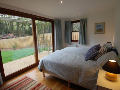 A bedroom with a bed pillows bedside table lamp sliding glass door and window at Orchard Retreat in Sidmouth